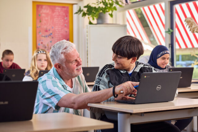 Leraar helpt met behulp van digitaal open leermateriaal een kind met een les.