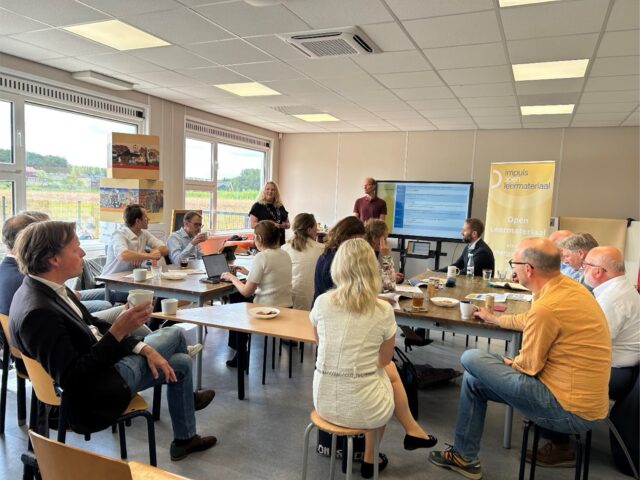 Betrokkenen bij het Groeifondsprogramma bijelkaar in een klaslokaal luisterend naar de presentatie van Impuls Open Leermateriaal.