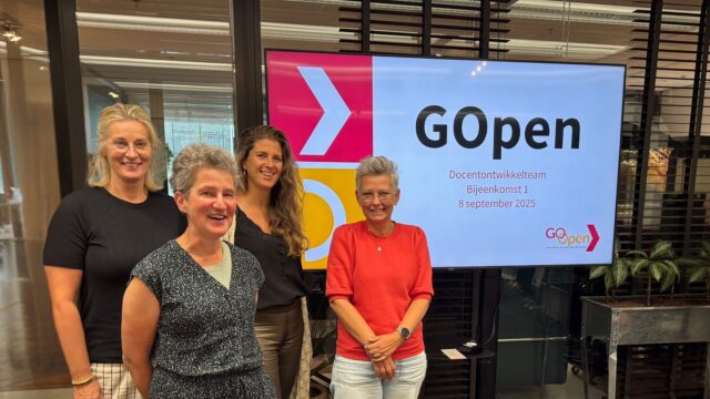 Vier mensen die deelnemen aan de DOT staan voor het digibord waarop de begin slide van de GOpen bijeenkomst te zien is.